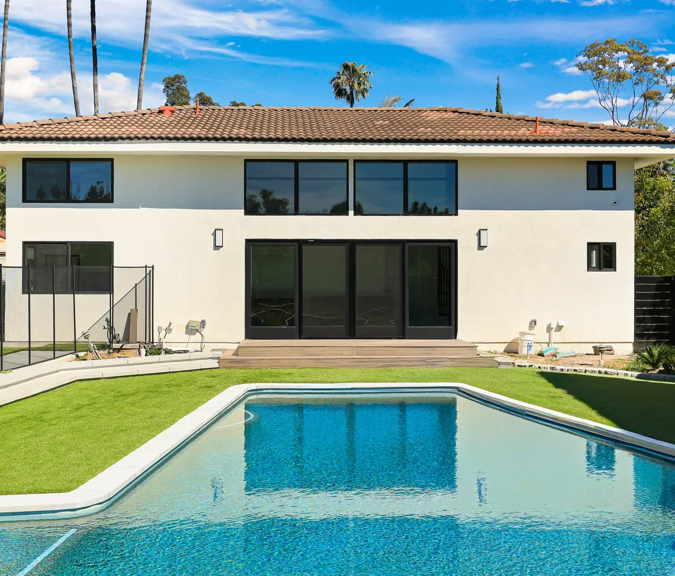 Two-storey stucco house with a tiled roof behind a pool and lawn