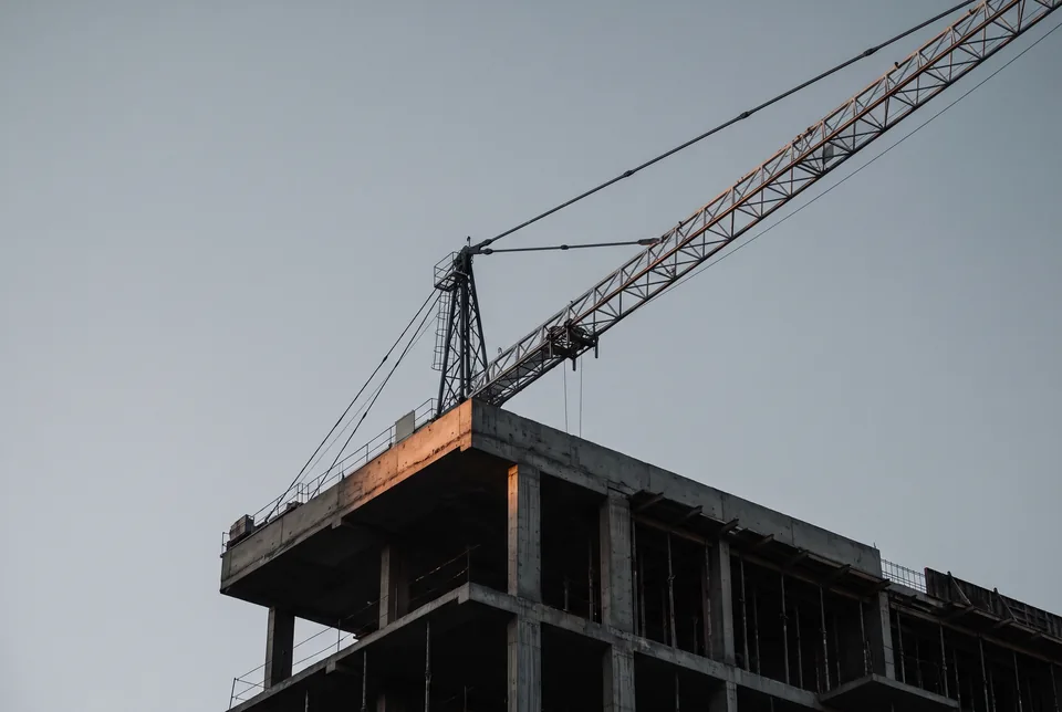 A tower crane above the top floors of a concrete frame against a pale dawn sky