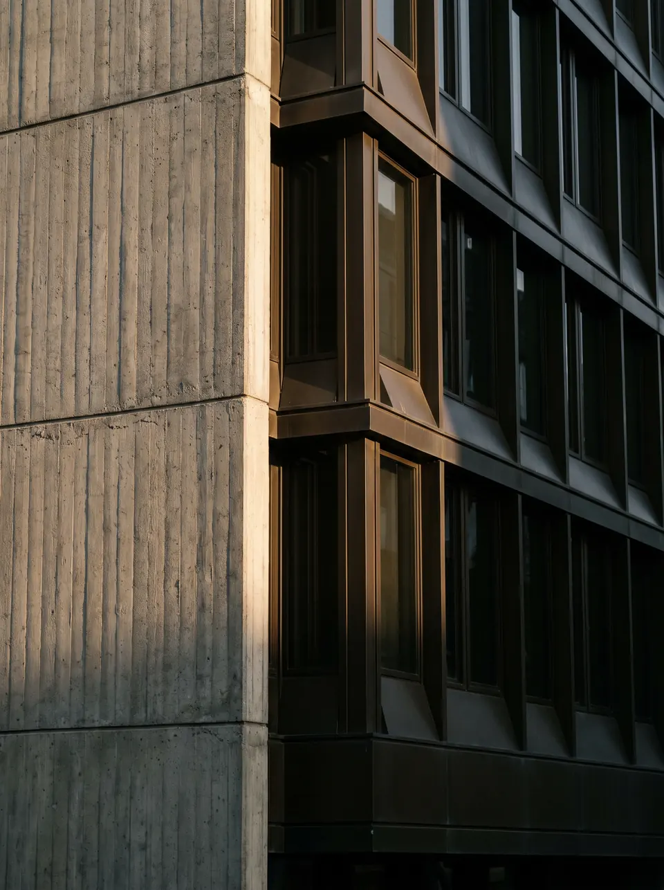 A building corner where board-formed concrete meets a run of dark window reveals