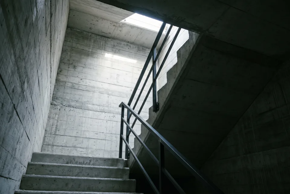 Daylight falling across the treads of a cast-concrete stair core