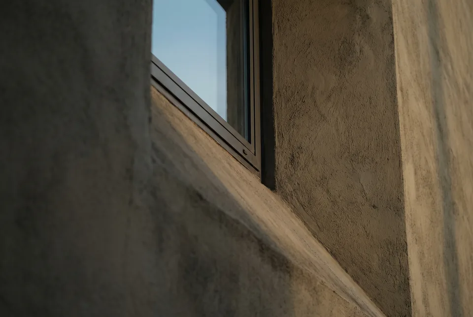 A deep stucco window reveal with a dark frame and a sliver of pale sky